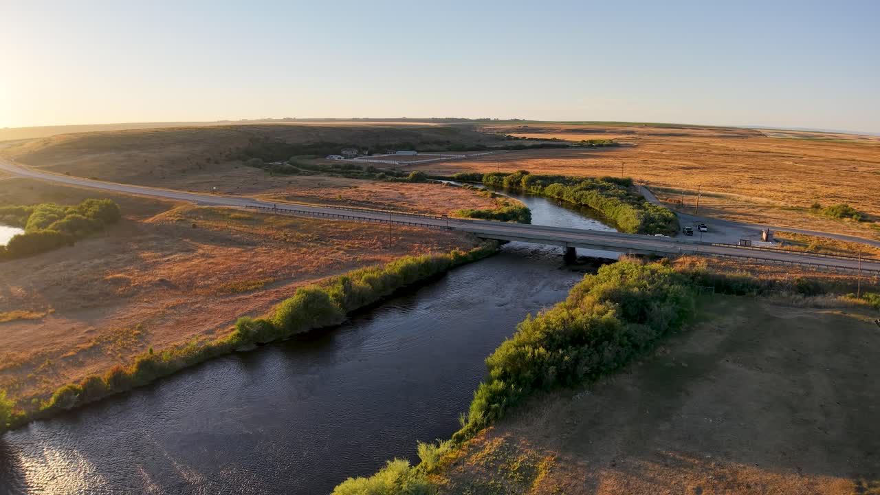 Ilmakuva mutkittelevasta joesta ja viljelysmaista auringonlaskun aikaan, kultaisen valon heijastuessa vedestä ja vihreiden puiden reunustaessa rantoja.