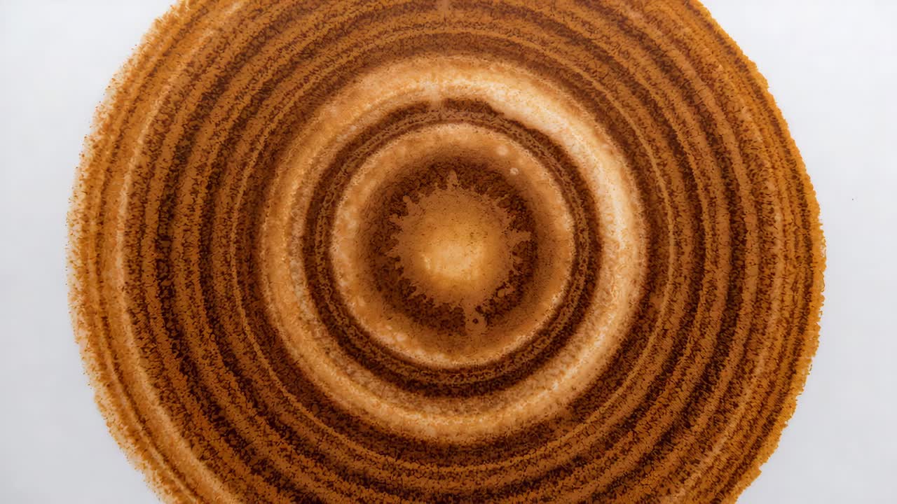Showing frames of large granular brown concentric rings shifting tone and texture on white base