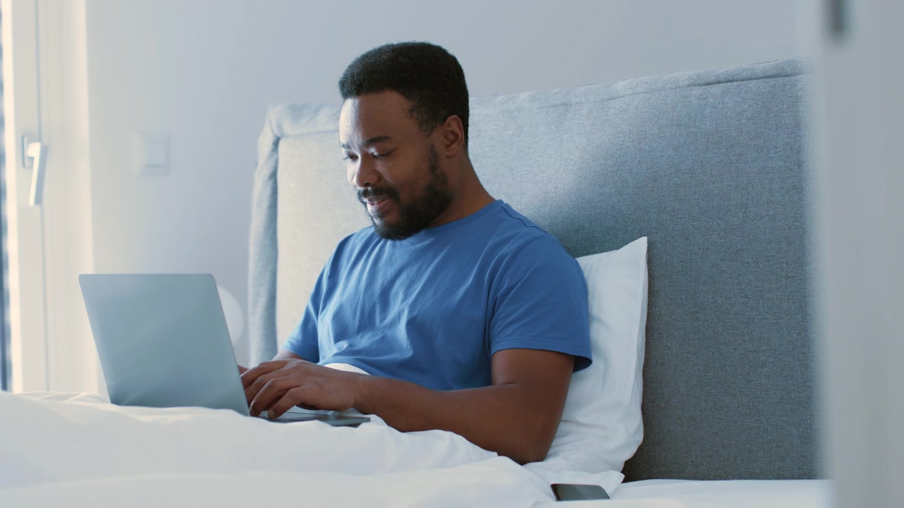 Young Man Working on Laptop While Sitting in Bed