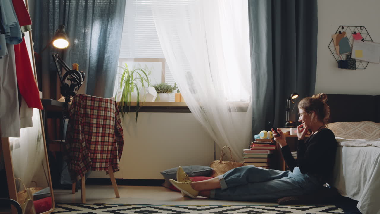 침실 바닥에 앉아서 스마트폰을 사용하는 여자