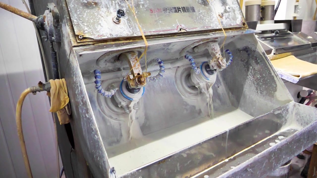 Industrial polishing and grinding machine in a lens factory, using water jets for cooling during high-precision processing. Jiangsu Province, China.