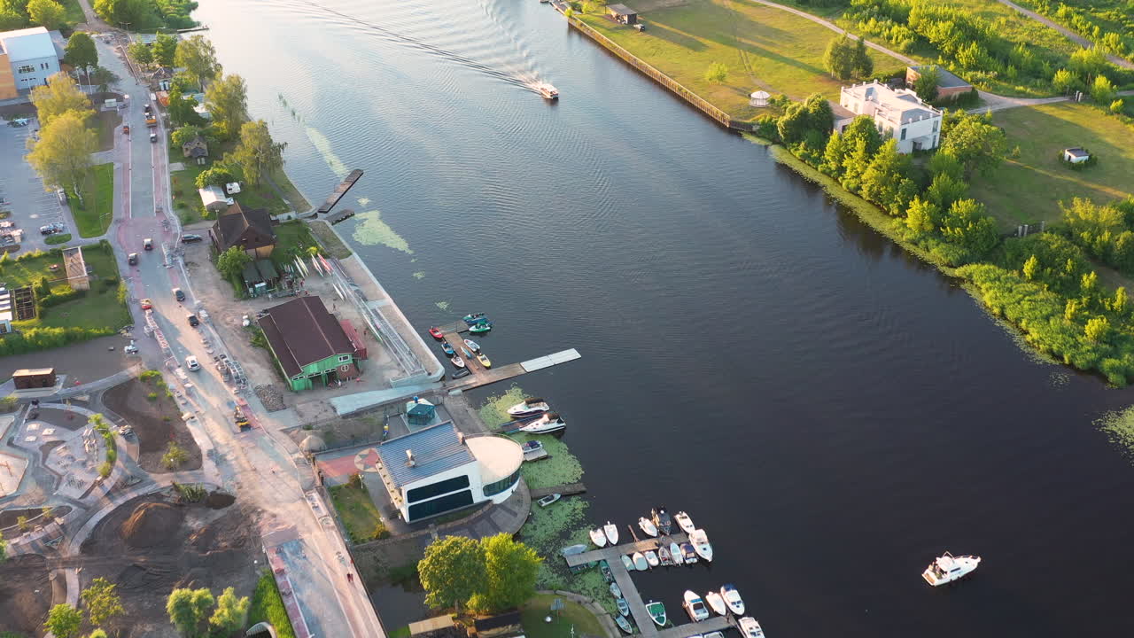 Aerial view of riverside street with boats docked along the waterfront marina on golden hour