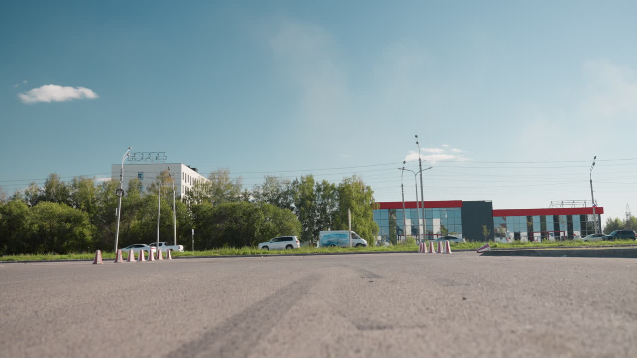 Rear view of biker walking on pavement holding leather jacket in hand wearing black leather outfit under bright daylight with urban background of cars trees and buildings
