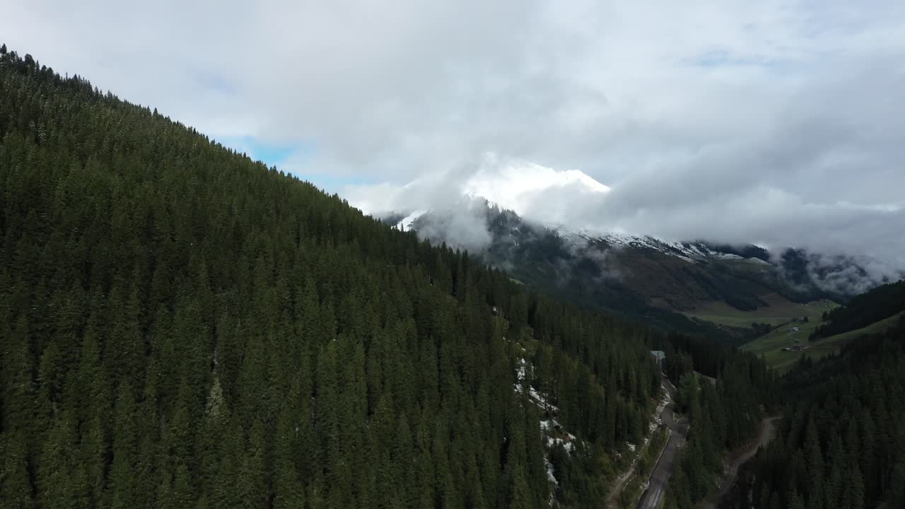 A dramatic aerial view of fog drifting through the snow-covered Zillertal Valley surrounded by coniferous forests.