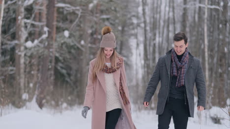 in the winter snowy forest, young men and women dressed in coats and scarves are walking and having fun. loving couple spend together valentines day.