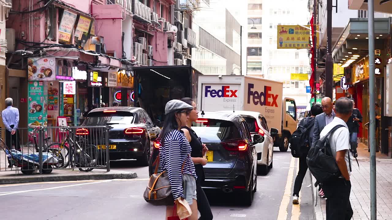 People and cars navigate a tight street lined with colorful shops and signs.
