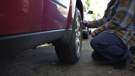 a caucasian male checks the tire pressure on a red car