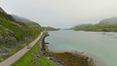 Cinematic-aerial-shot-of-a-car-driving-along-a-scenic-road-on-the-famous-Lofoten-Islands-in-Norway,-Europe