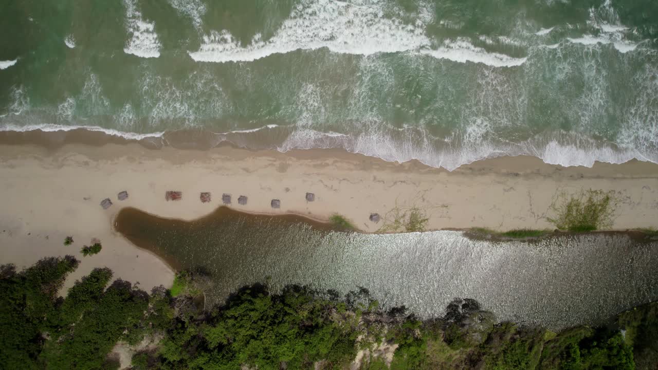 A beach with sea waves crashing, close to a lagoon surrounded by nature, aerial view