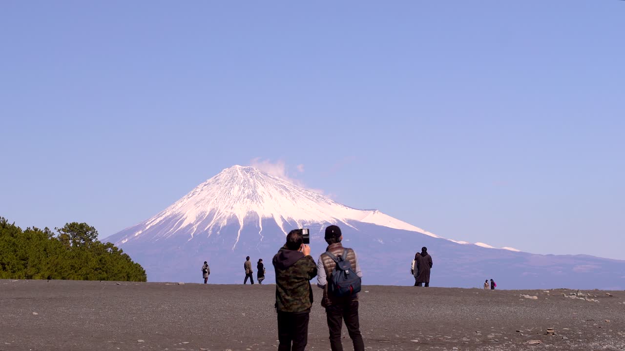 gente en la playa tomando fotos con el monte fuji altísimo en segundo plano