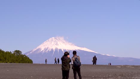 Gente-En-La-Playa-Tomando-Fotos-Con-El-Monte-Fuji-Altísimo-En-Segundo-Plano