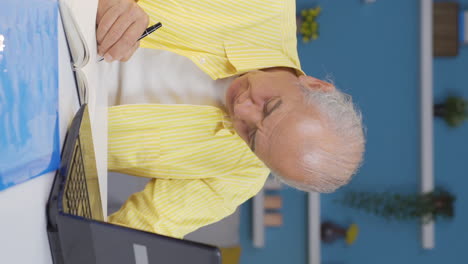 Vertical-video-of-Home-office-worker-old-man-taking-notes,-jotting-down-information.