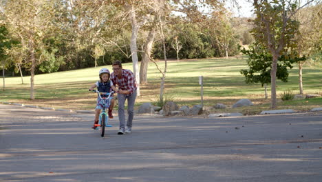 padre enseñando a su hija a montar una bicicleta en un camino rural