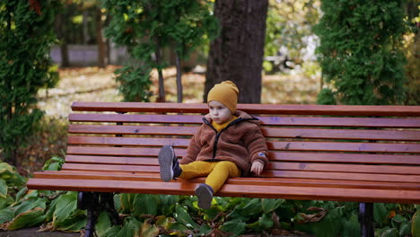beautiful toddler boy sits on the bench waving his foot. calm baby boy resting in the park.