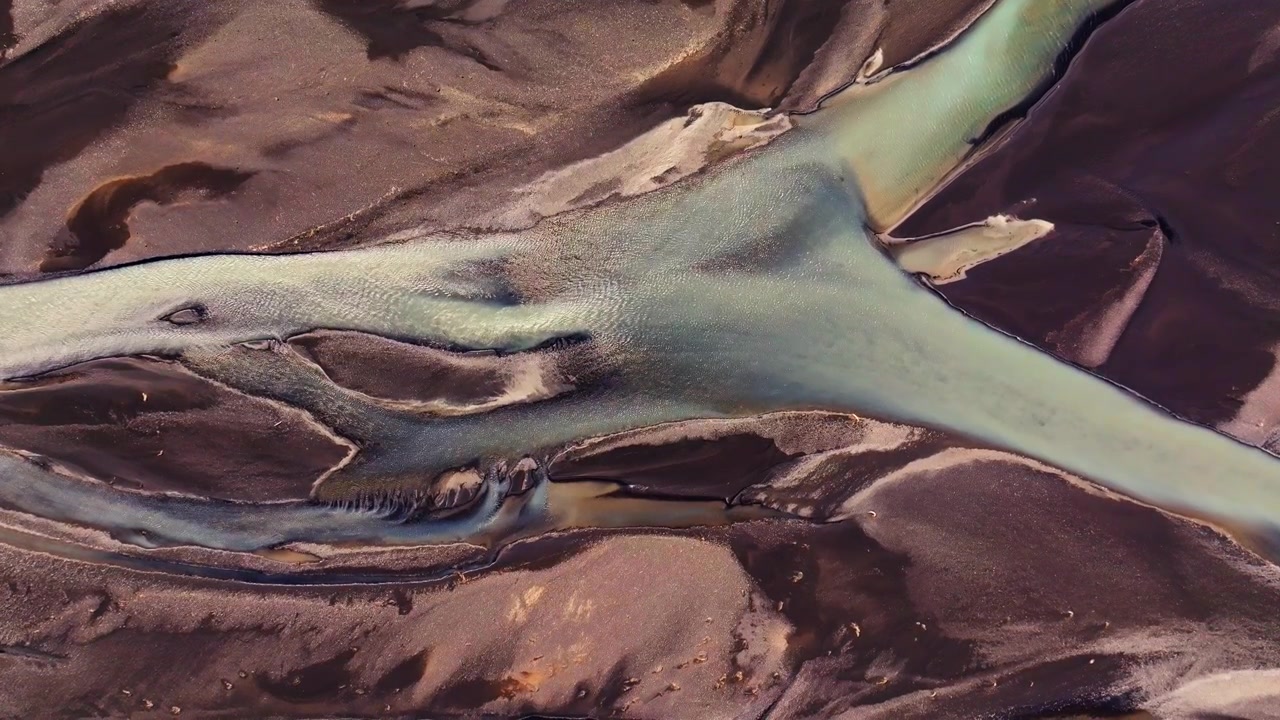 Prospettiva aerea astratta di corsi d'acqua glaciali islandesi che si ramificano e si ricongiungono. Il flusso dinamico dell'acqua di disgelo scava canali in costante mutamento attraverso la terra vulcanica.