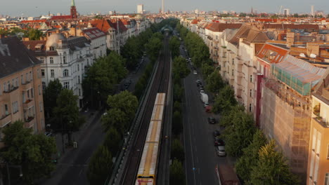 Forwards-tracking-scan-train-driving-in-wide-street-on-large-city.-Roofs-of-buildings-lit-by-bright-morning-sun.-Fly-towards-Fernsehturm-TV-tower.-Berlin,-Germany