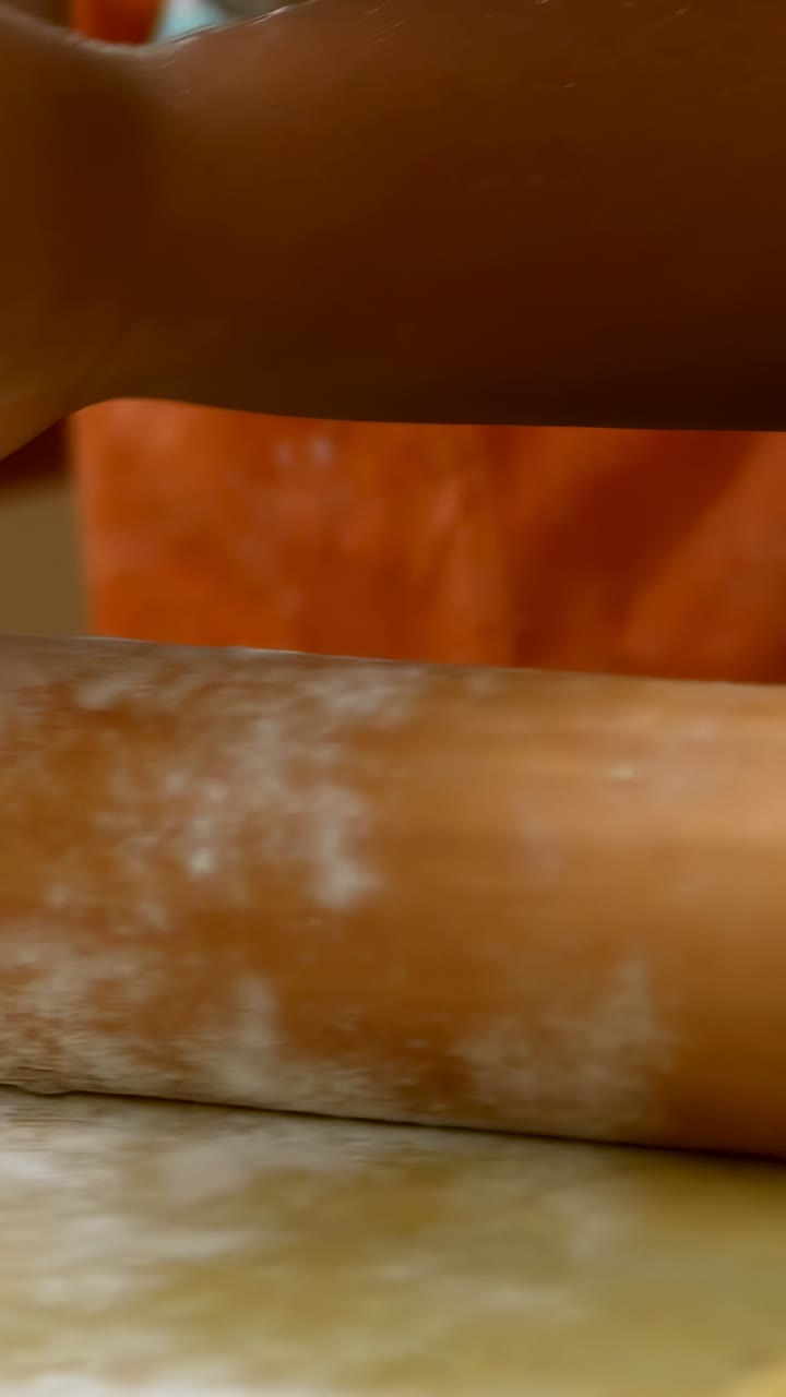 Video verticale: Mattarello che entra, mani che impastano la pasta per cuocere a casa, grembiule arancione, ciotola blu.