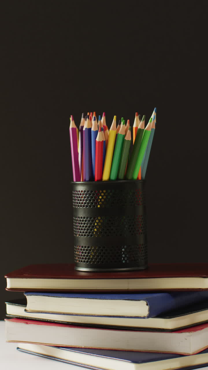 video vertical de una pila de libros, lápices de colores y tendido sobre un fondo negro