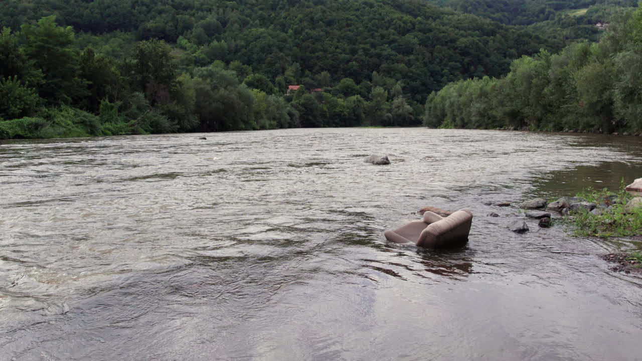 Old sofa dumped in flowing river water symbolizing pollution and environmental damage