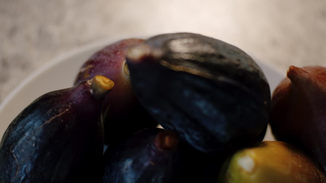 Close up of fresh ripe figs fruit in white bowl on marble kitchen top