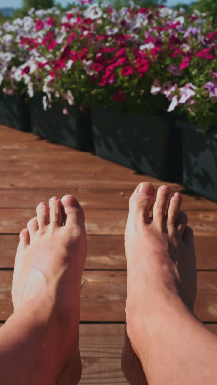 Piedi che si rilassano su una terrazza in legno con fiori in una giornata di sole