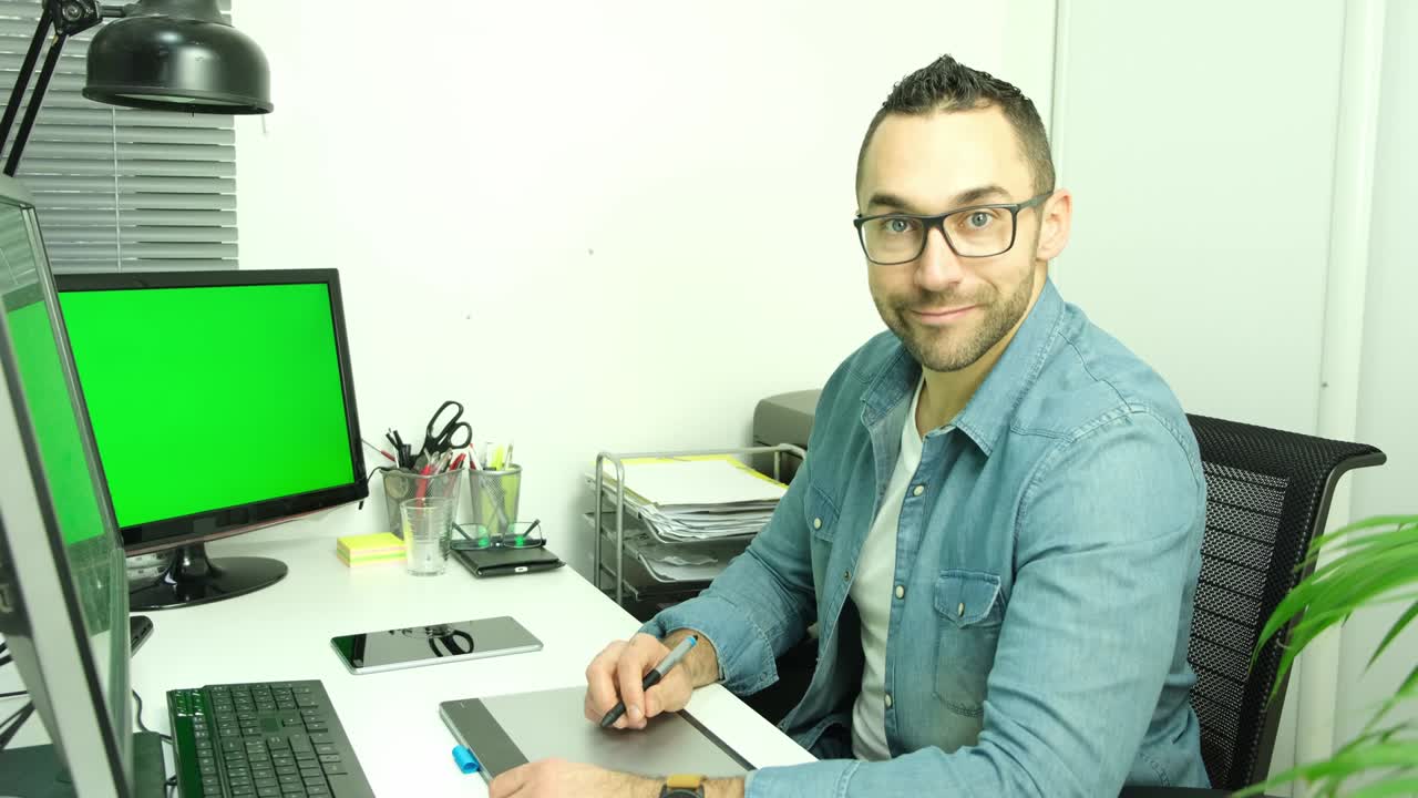 hombre guapo artista gráfico joven trabajando en la oficina con computadora y tableta gráfica 4k 50fps imágenes chromakey pantalla verde