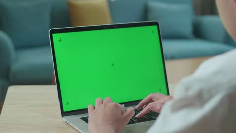 primer plano de un estudiante asiático escribiendo en una computadora de pantalla verde en casa
