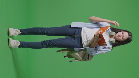 full body of asian teen girl student with a backpack reading book and having a headache while standing in the green screen background studio