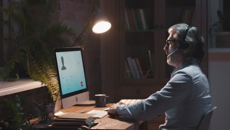 senior man working remotely on a video call in his home office at night