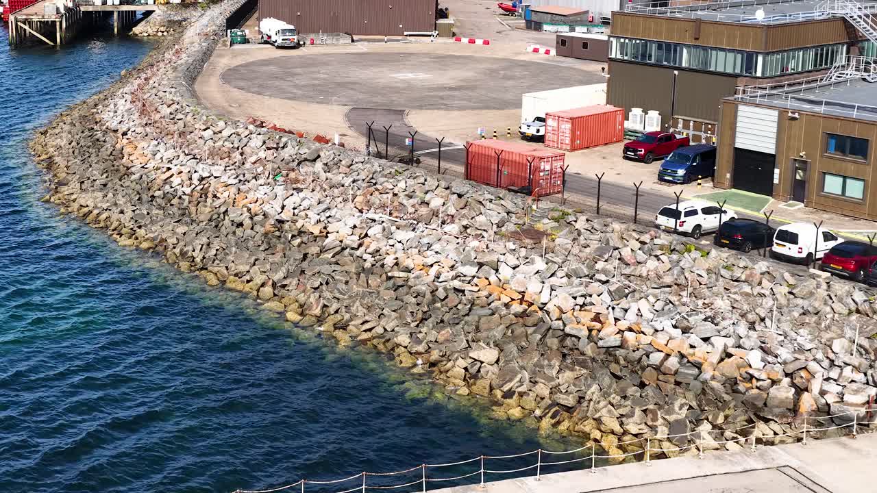 Green and white vessel docks at industrial pier, sunny daylight, aerial camera movement, coastal environment