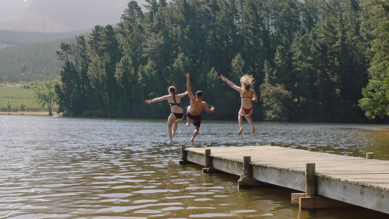 amici felici che saltano dal molo nel lago che si spruzzano in acqua che si godono la libertà che si divertono avventura estiva in vacanza