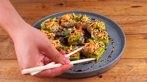 Close-up-of-hands-with-chopsticks,-taking-an-avocado-sushi-roll-from-a-blue-plate