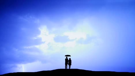 the couple with umbrella standing on a hill against the background of lightning