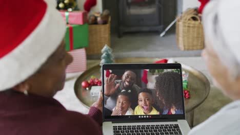 Two-diverse-senior-female-friends-using-laptop-for-christmas-video-call-with-family-on-screen