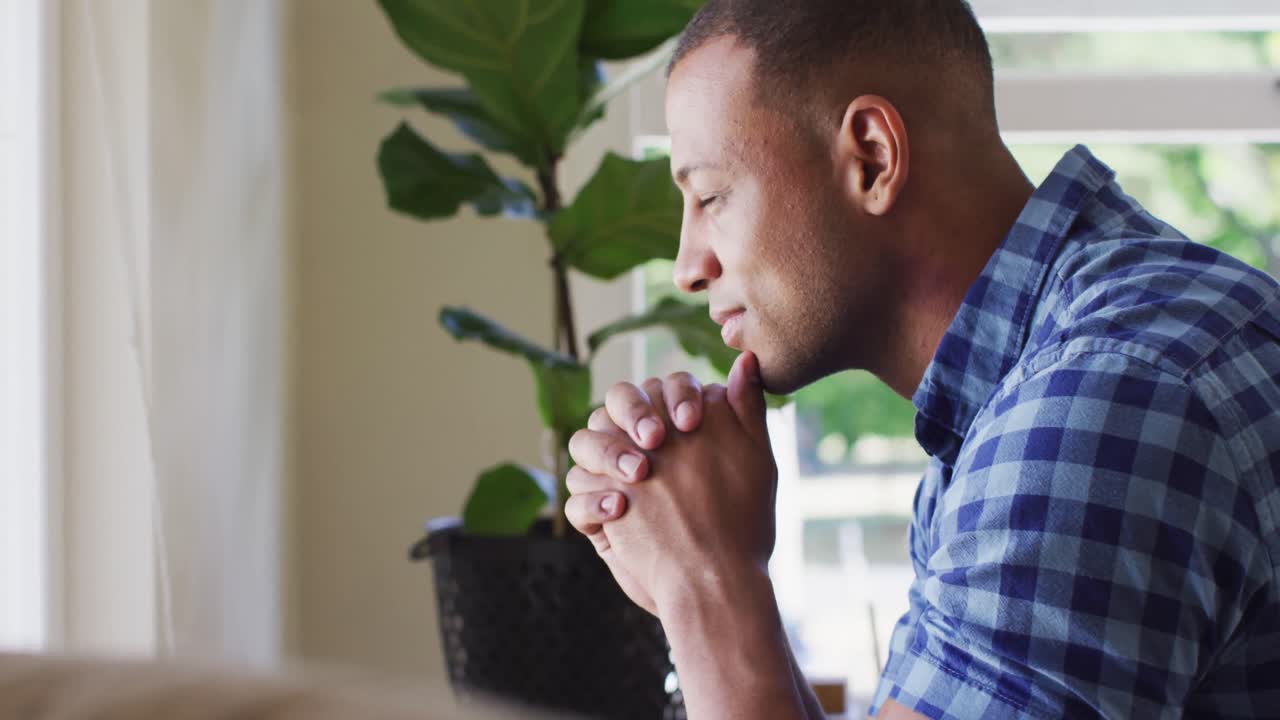 Side view of thoughtful biracial man sitting and looking outside window
