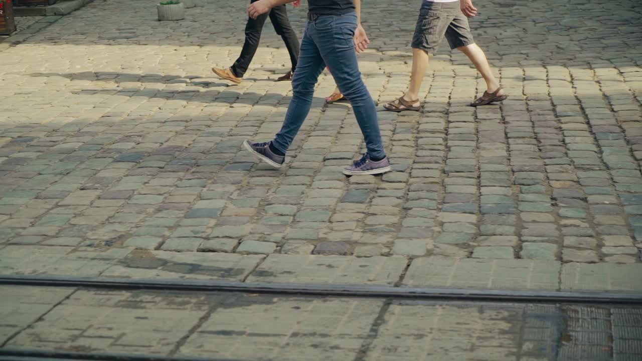 Pedestrians crossing the main street on the old pavement in Lviv. Movement of people's legs on the road in ancient city after the rain.