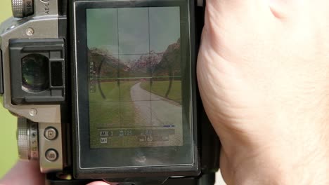 Close-up-of-the-back-of-a-camera-as-a-photography-level-the-camera-in-a-vertical-orientation-with-a-road-leading-into-the-mountains-in-the-alps