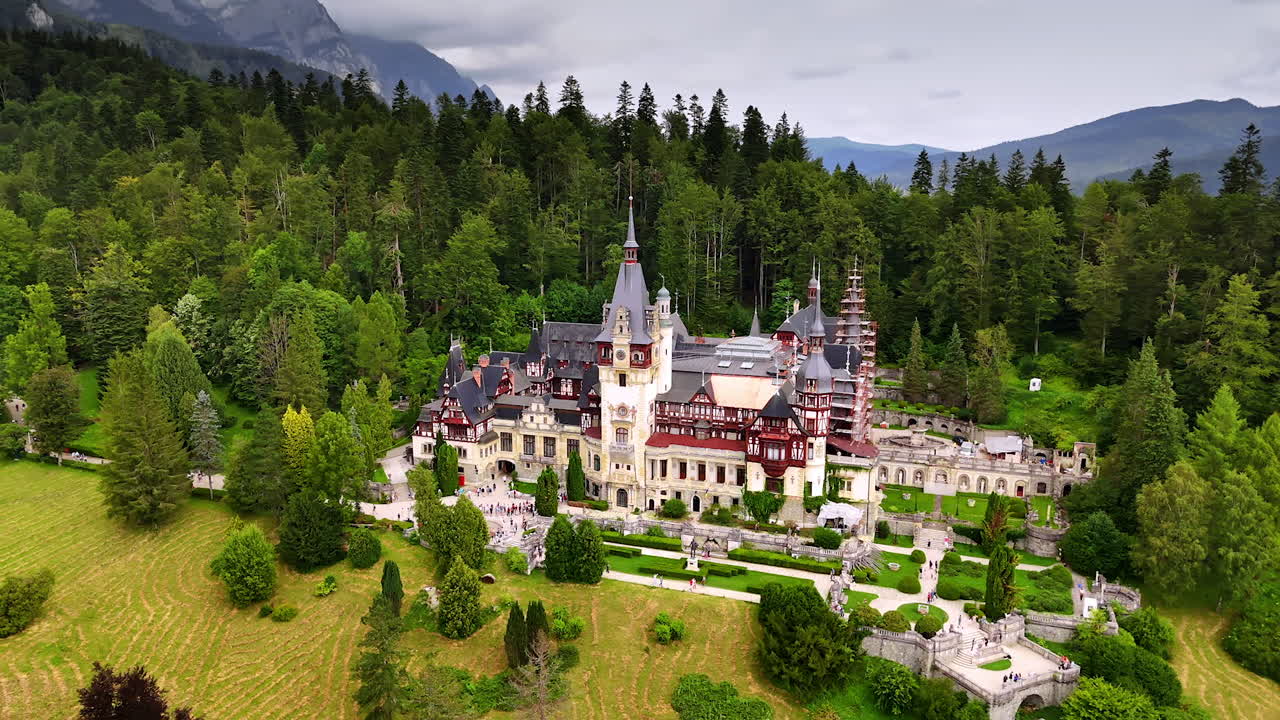 Striking Peles Castle, Prahova County, Romania against lush pine tree wood. Grey clouds touch the mountain tops at backdrop