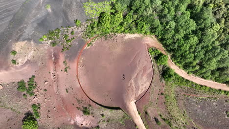 Aerial-overhead-ascending-view-of-two-people-and-dog-meeting-in-circled-shaped-volcanic-area