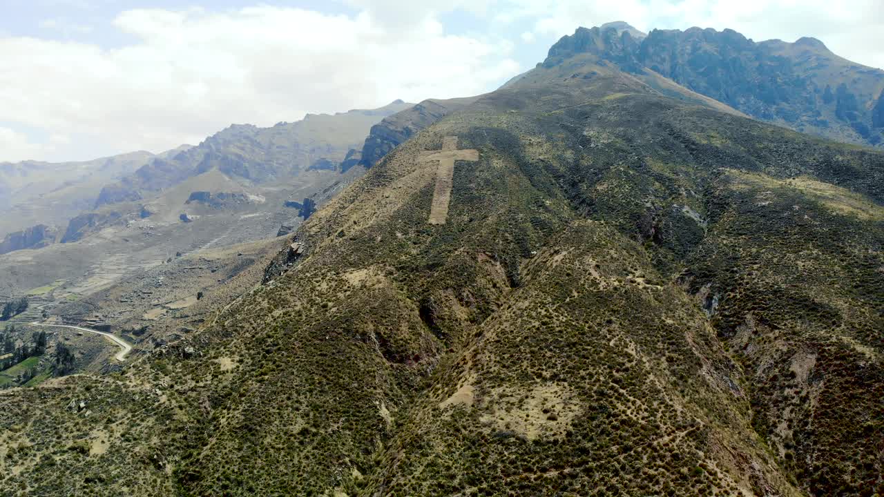 toma aérea hacia atrás de un enorme crucifijo católico hecho a mano en la ladera de la montaña en chivay perú