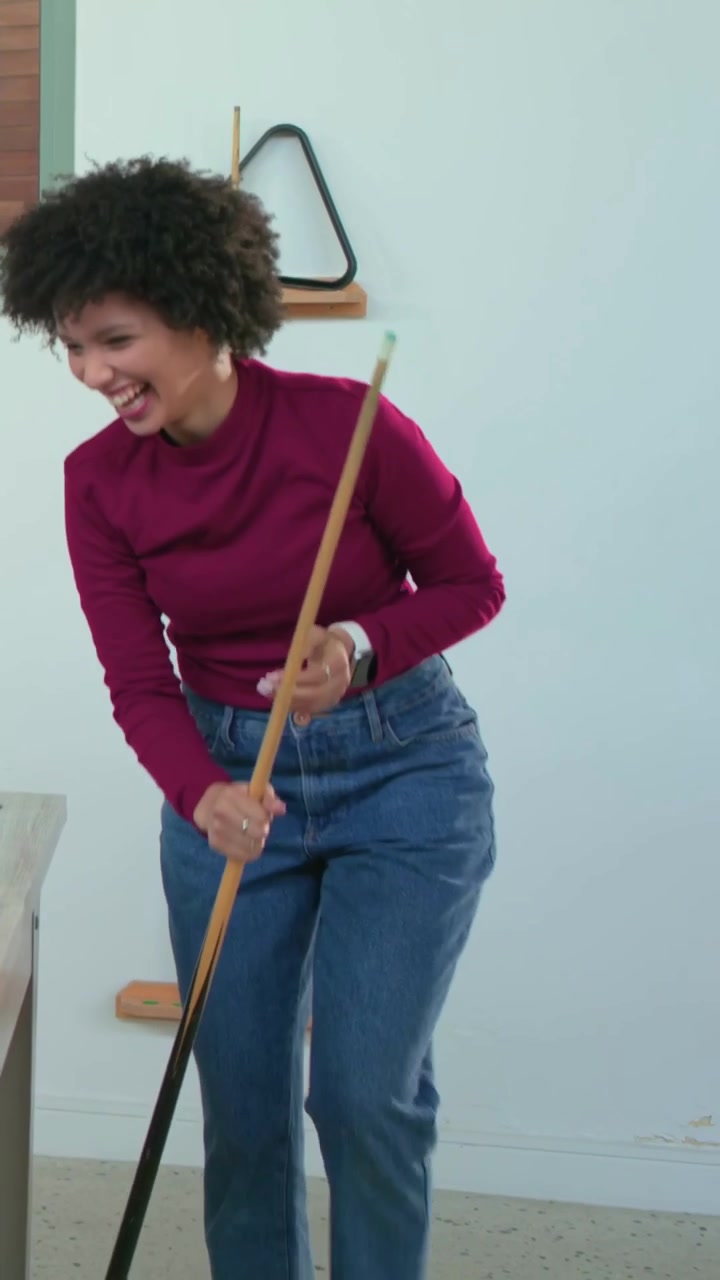 Video vertical: Mujer celebrando con blusa granate, haciendo girar un taco de billar después de un tiro ganador en casa.