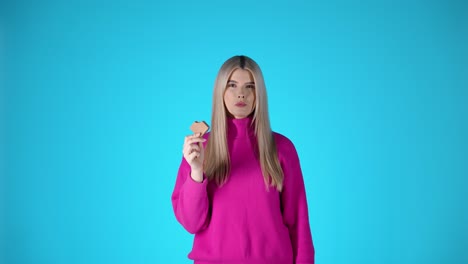 Blonde-Frau-Mit-Rosa-Pullover-Nimmt-Ein-Stück-Schokoladenkeks,-Blauer-Hintergrund