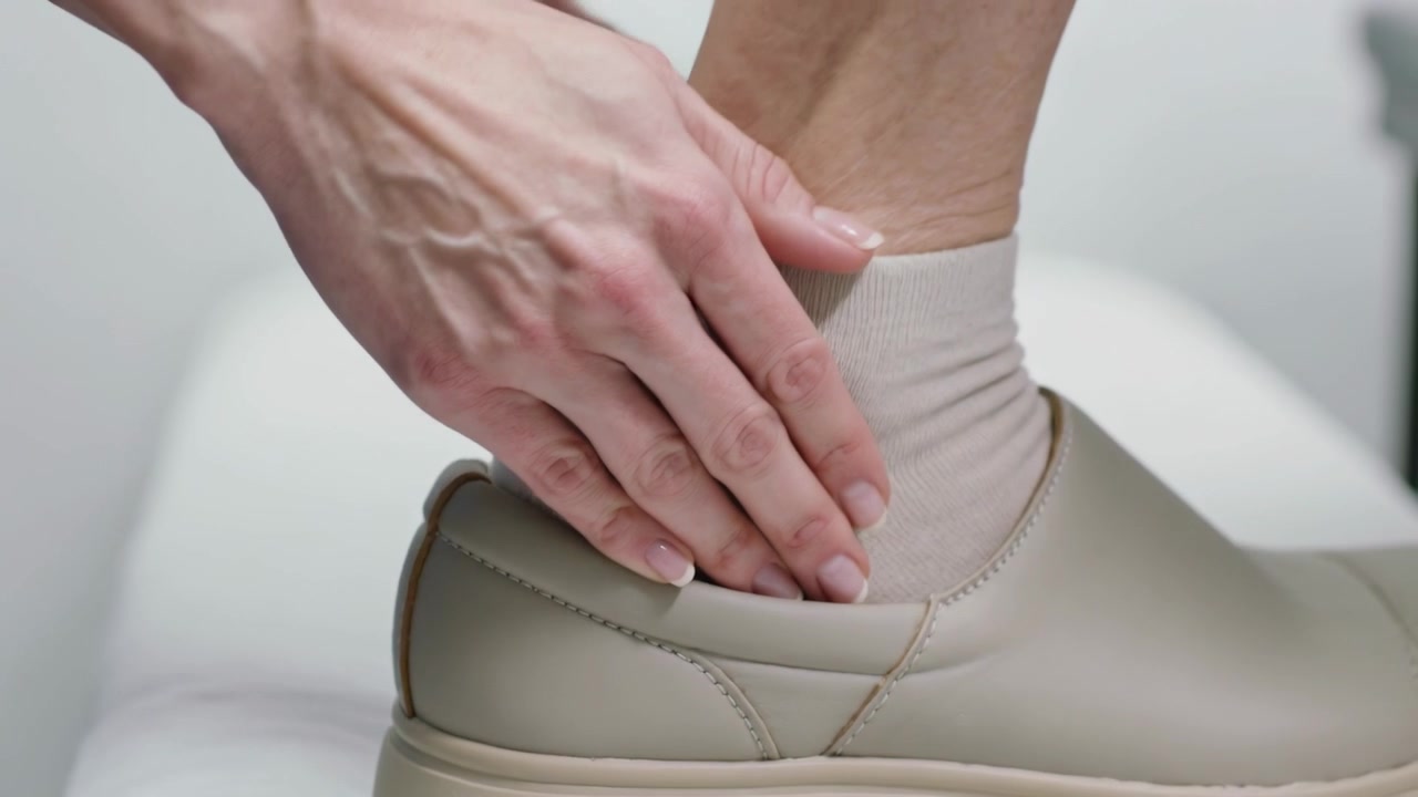 Guiding person's hand putting foot into beige slip-on shoe at studio, tucking sock for flush fit