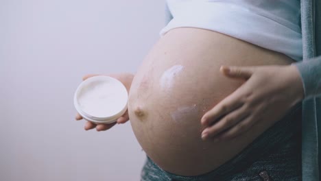 pregnant lady applies moisturizing lotion on tummy closeup