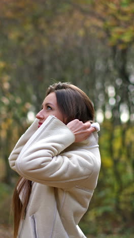 enjoying walk in the nature and beautiful autumn weather. brunette raising the collar of her jacket and smiling into camera. vertical video