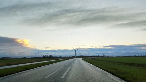 Molino-De-Viento-A-Lo-Lejos-Con-Un-Amanecer-Y-Coches-Acercándose-En-La-Carretera