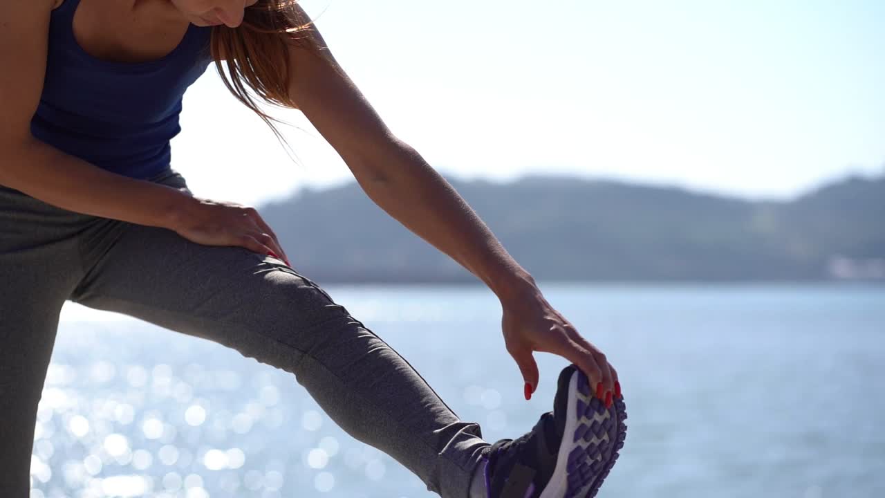 Sporty girl stretching leg at riverside