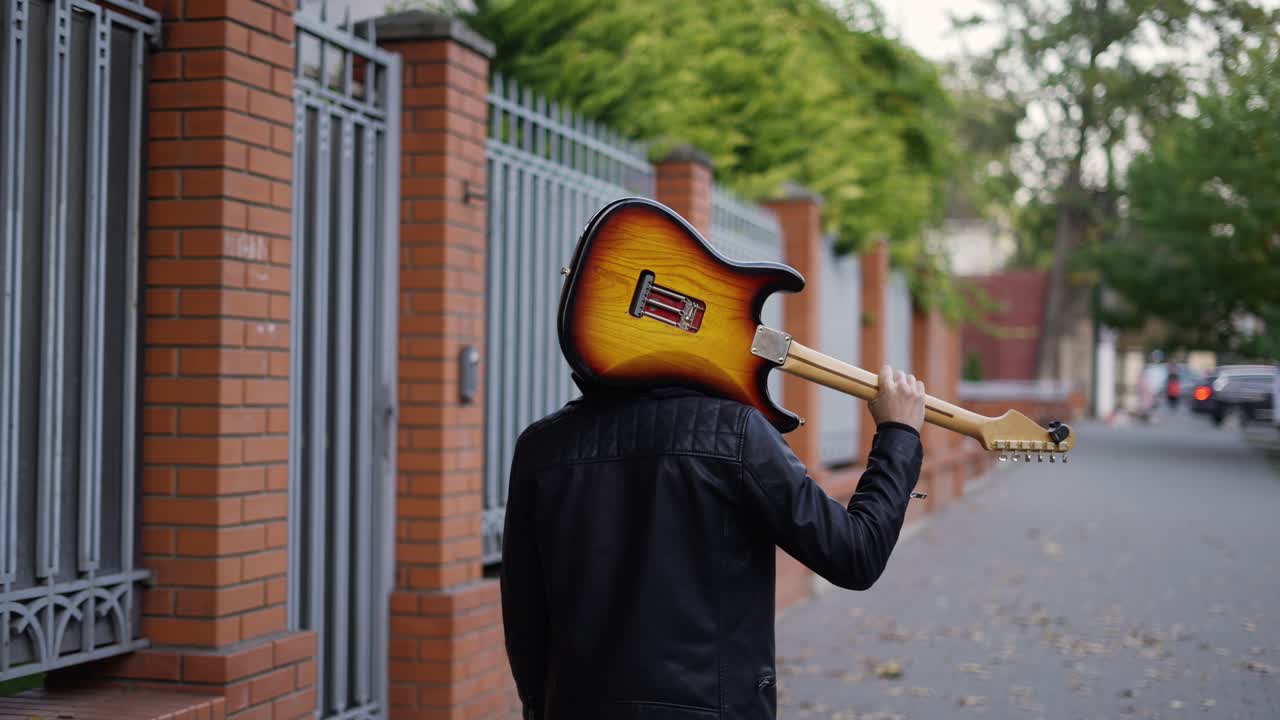hombre caminando por la calle con una guitarra en su hombro