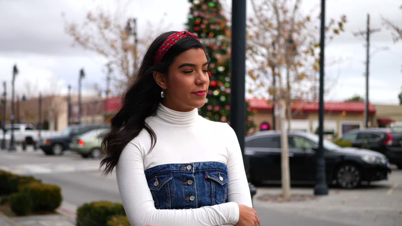 Una donna che cammina sul marciapiede in città facendo shopping natalizio con un albero decorato con ornamenti e luci festive al RALLENTATORE