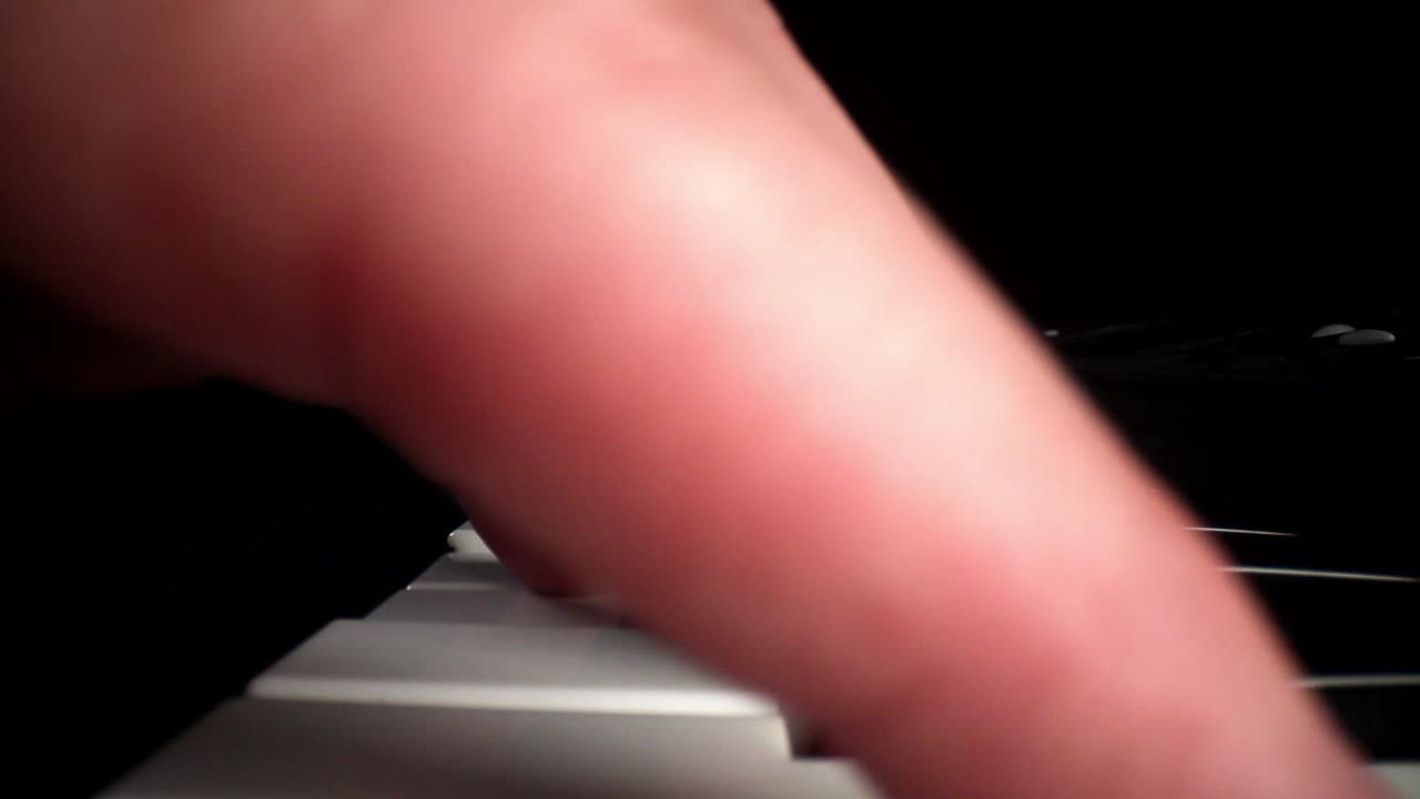 Wide angle macro of electronic keyboard - pushing across the top of the keyboard as hand plays notes, hand moves over the lens as it moves down the keys